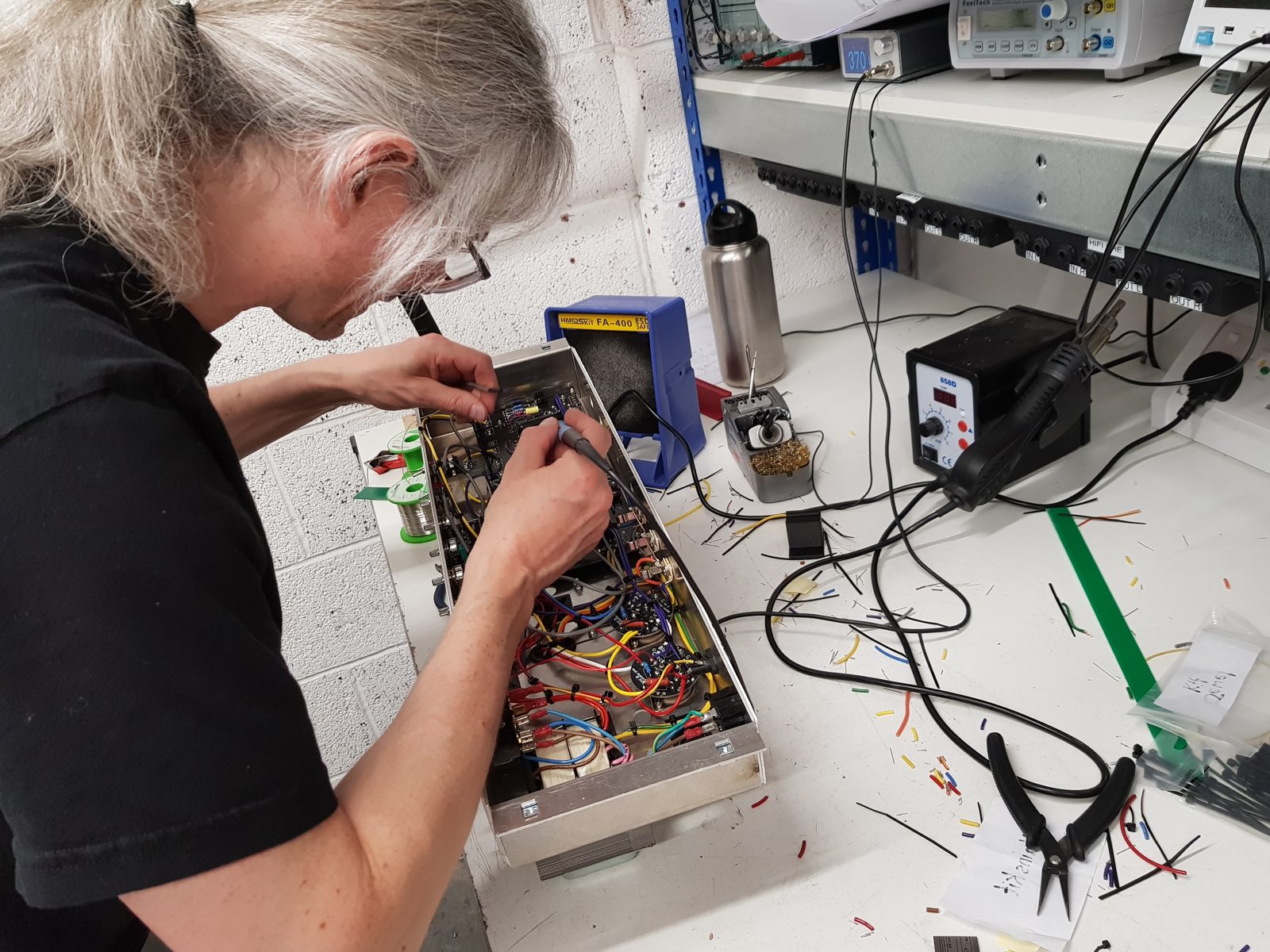 Close-up of hands soldering wires to a valve socket and circuit board inside a valve amp chassis