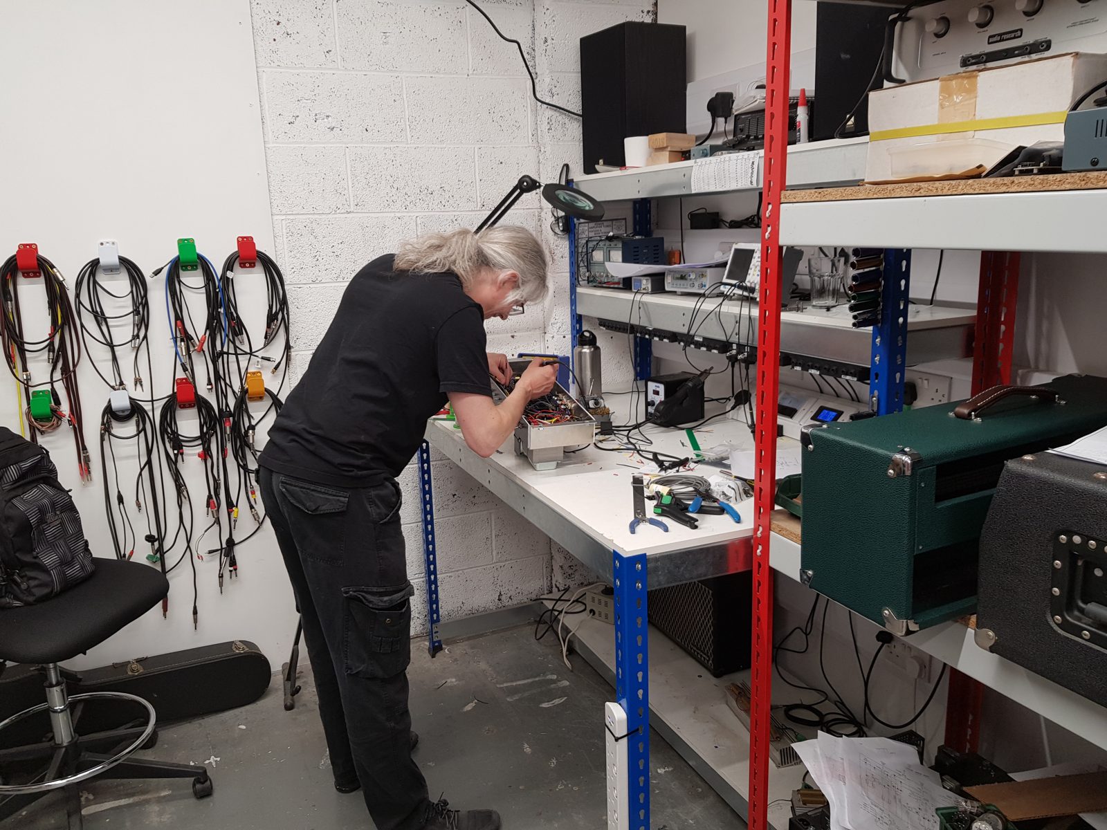 Builder soldering the wiring inside a valve amp chassis at a workbench in the Guitar Amp Academy workshop, Newark