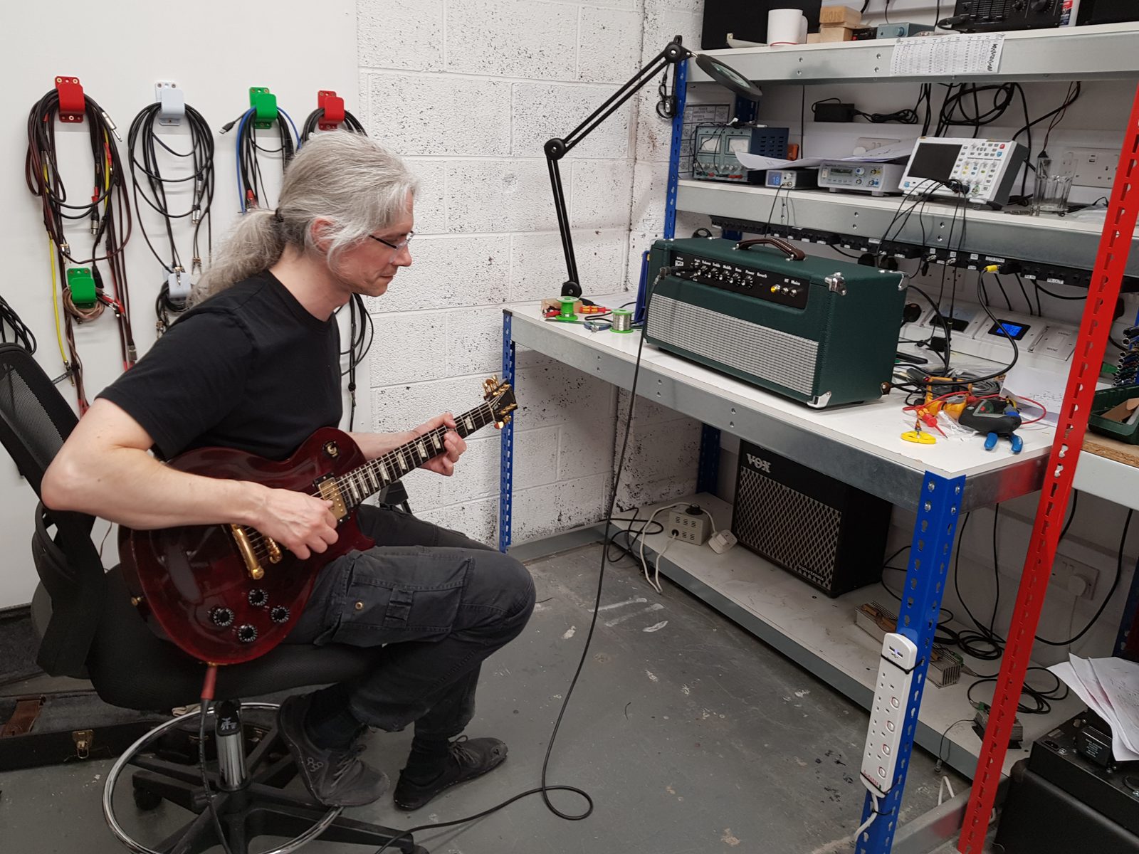 Builder playing a Les Paul through a finished green tolex valve amp head on the workbench